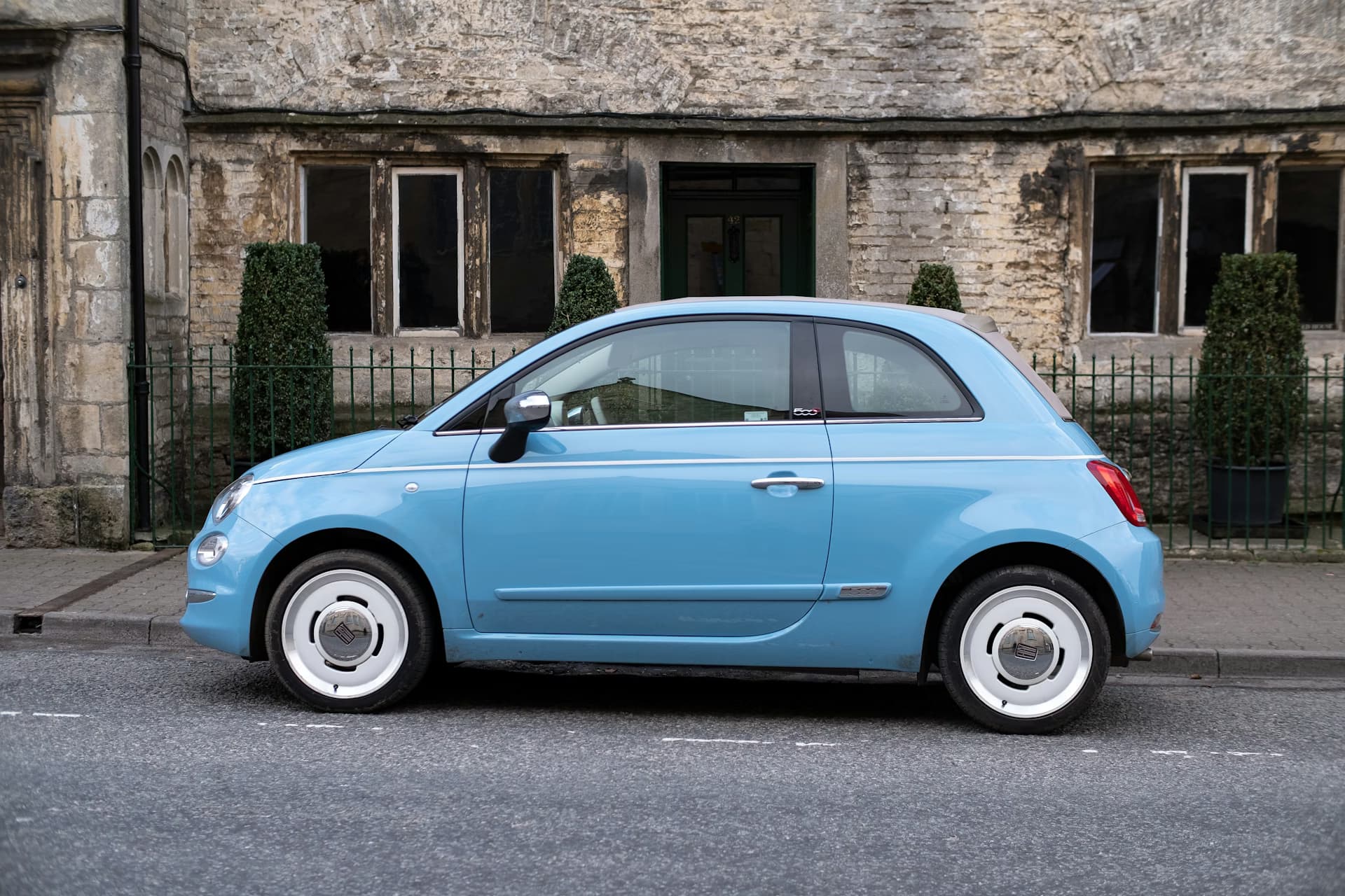 Light blue compact car parked on a street in front of a historic stone building — plan car rental in Sri Lanka before your flight